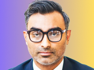 Man with short dark hair and beard wearing black glasses and a dark blazer, with a multicolored purple and yellow background.