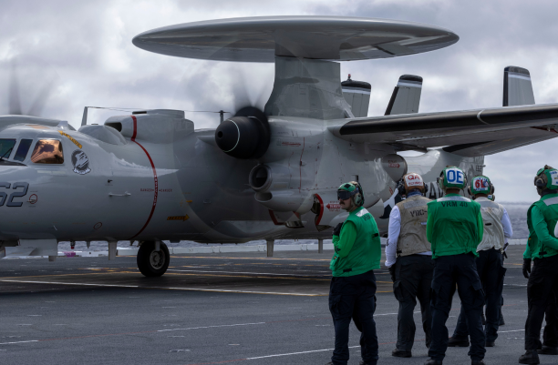 Technicians standing in front of a military aircraft on the tarmac