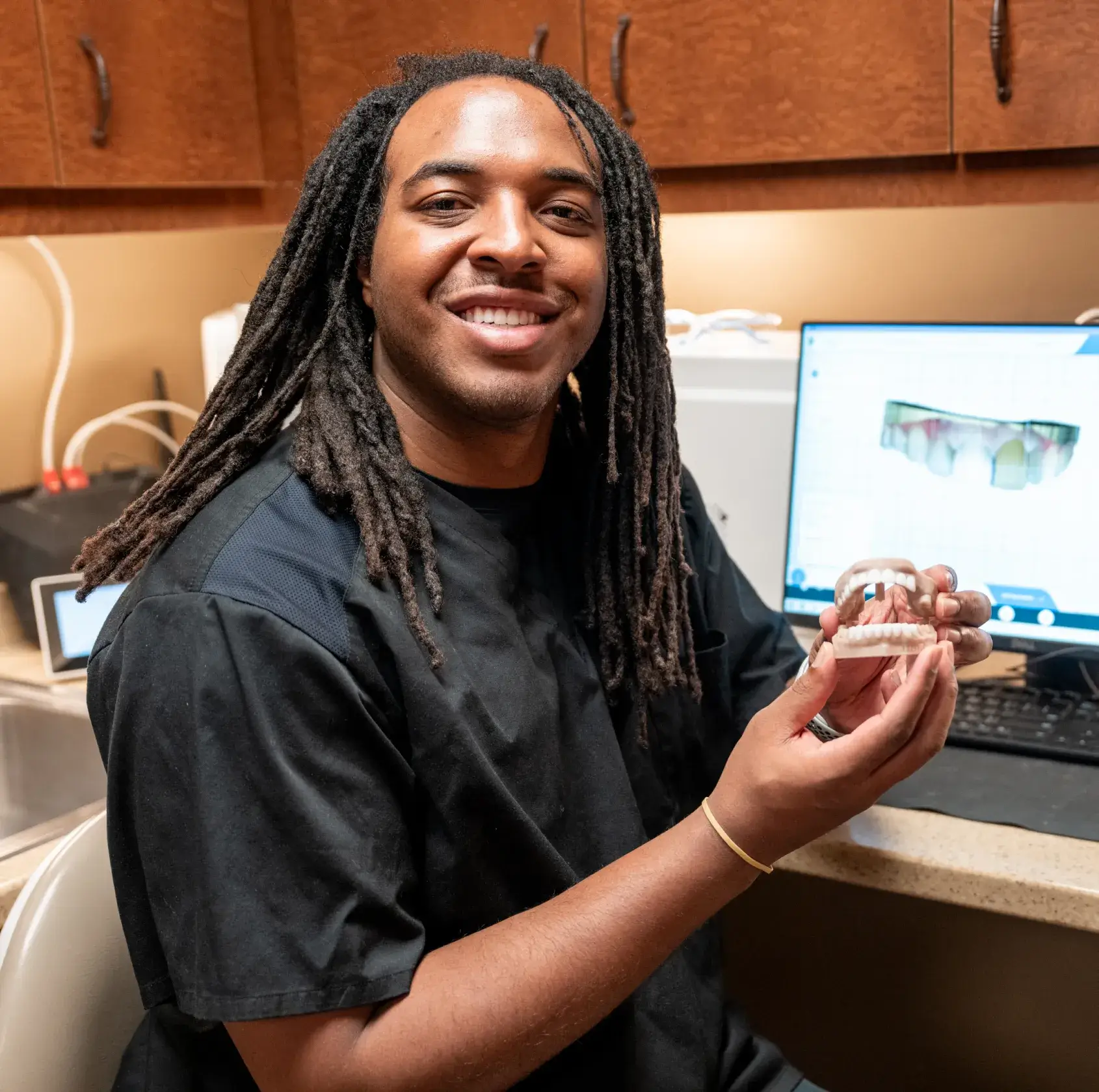 A person smiling and holding a dental mold in an office setting.