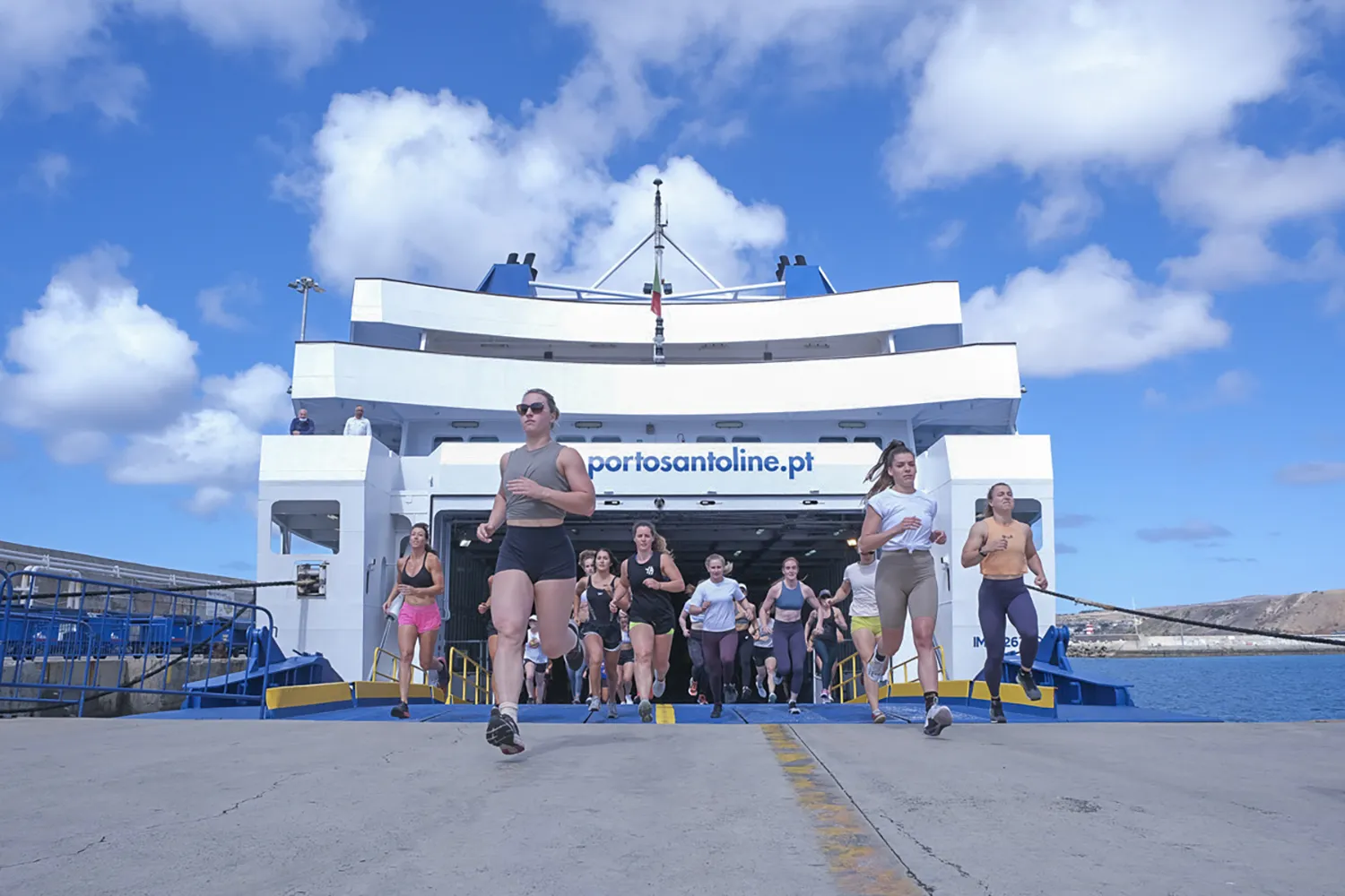 Group of women exiting a boat and running towards the start of a workout during the Madeira Games.
