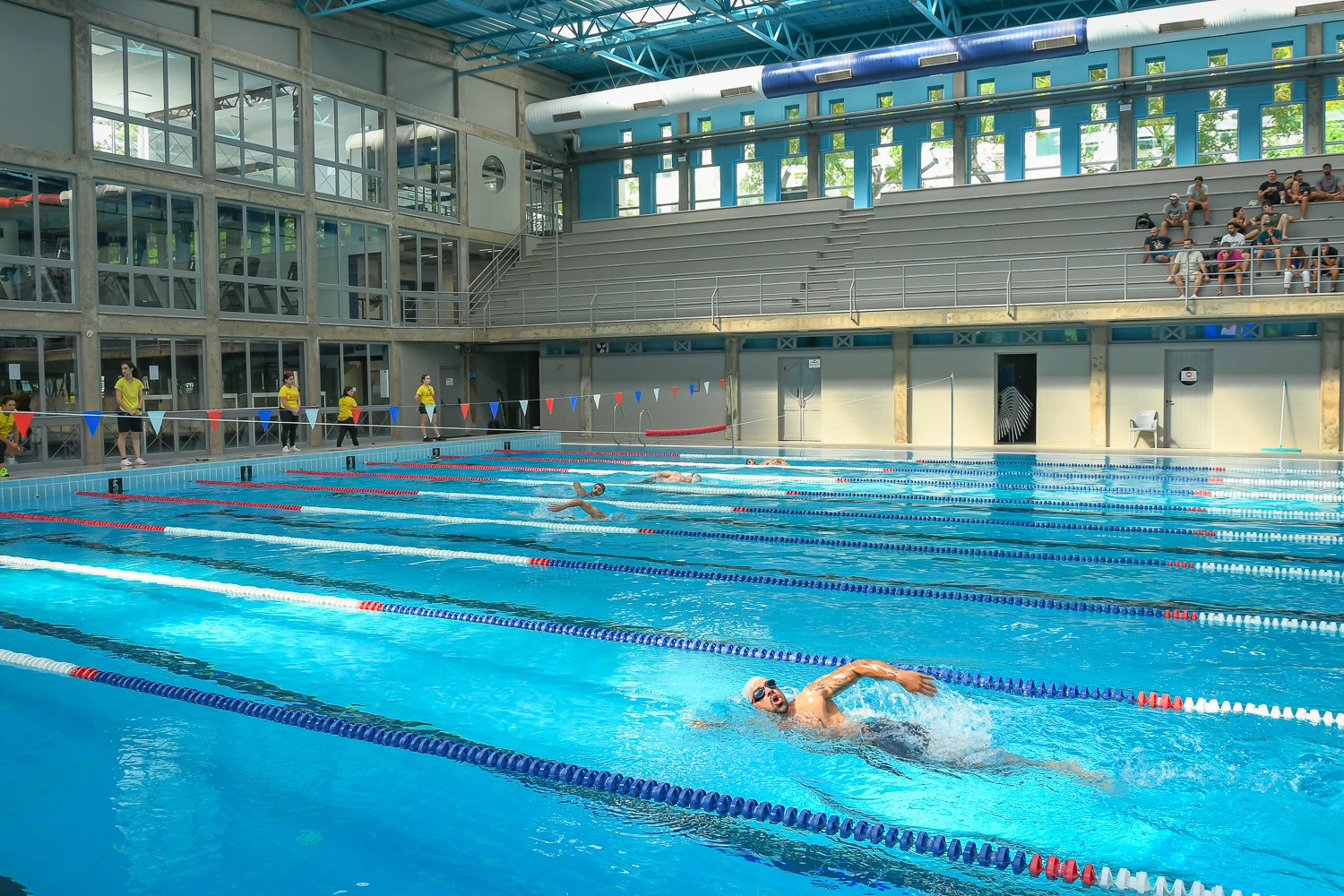 Group of athletes swimming laps in an indoor pool during a Madeira Games 2025 event.