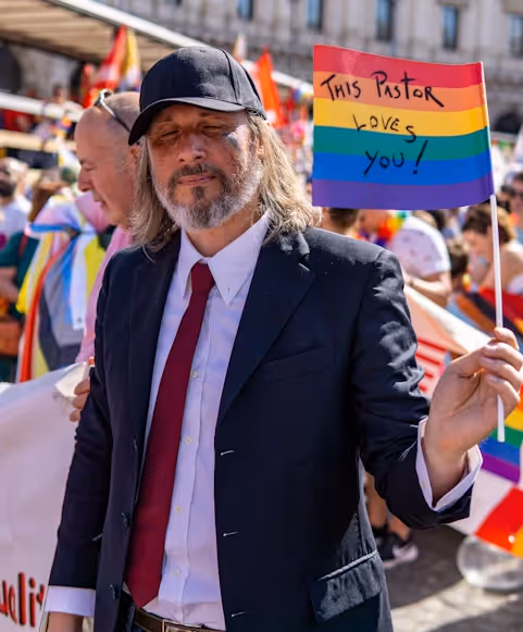 Man holding pride flag with the text "This Pastor Loves You"