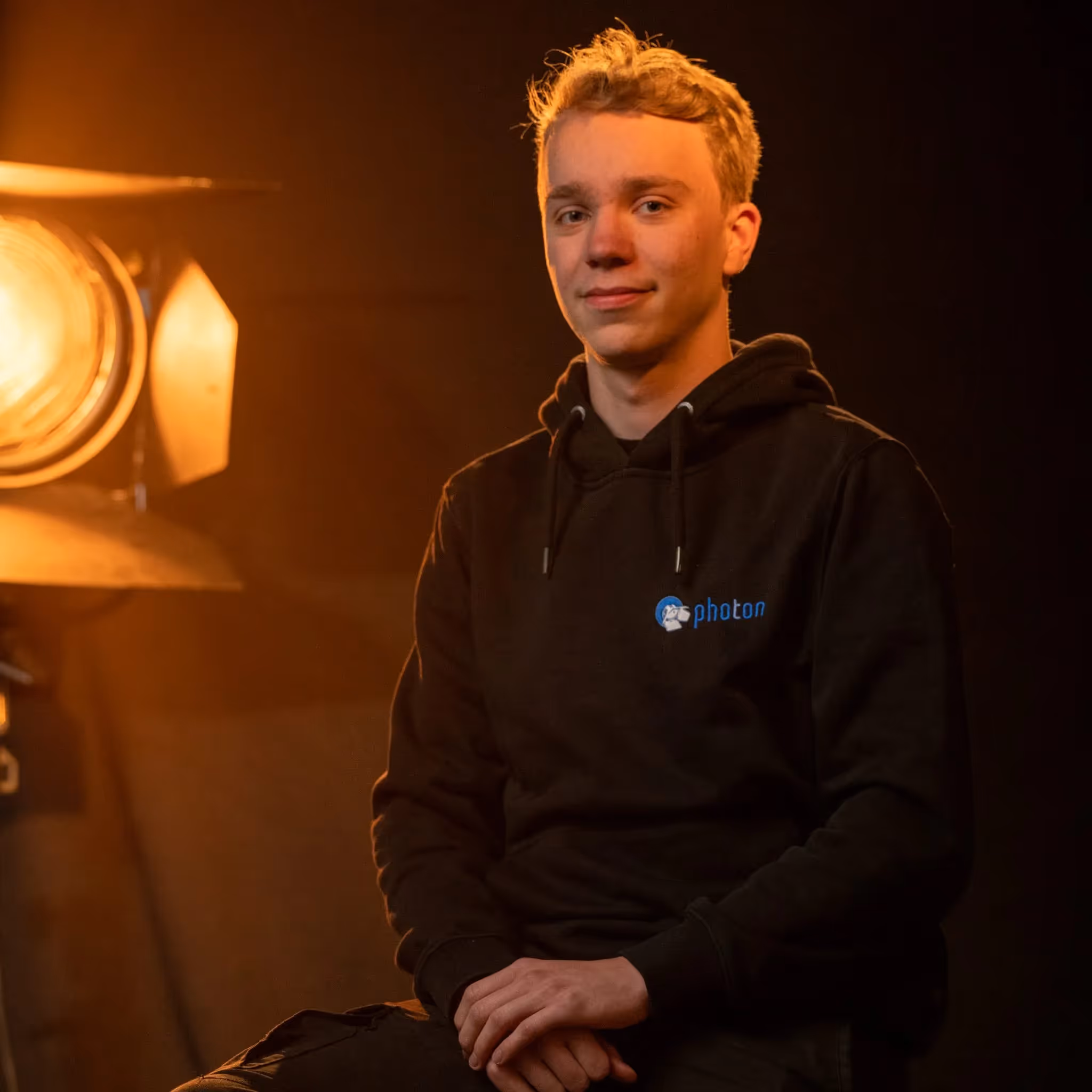 Alexander Schmitt mit Blonden Haaren und einem Schwarzen Pullover lächelt in die Kamera, eine Stufenlinse steht hinter ihm