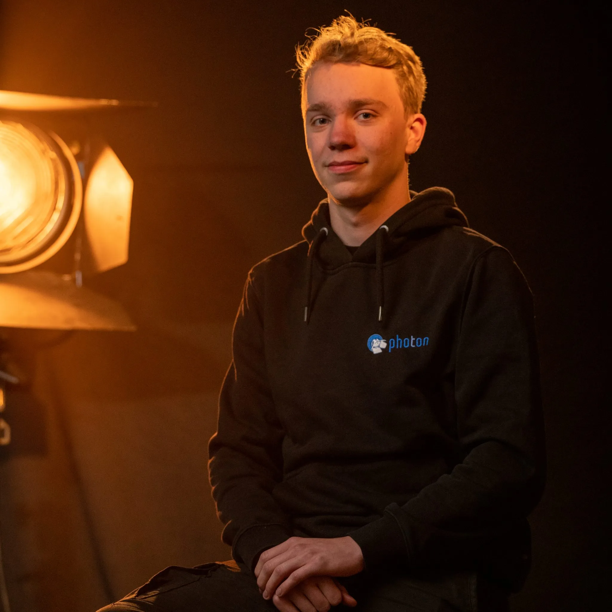 Alexander Schmitt mit Blonden Haaren und einem Schwarzen Pullover lächelt in die Kamera, eine Stufenlinse steht hinter ihm