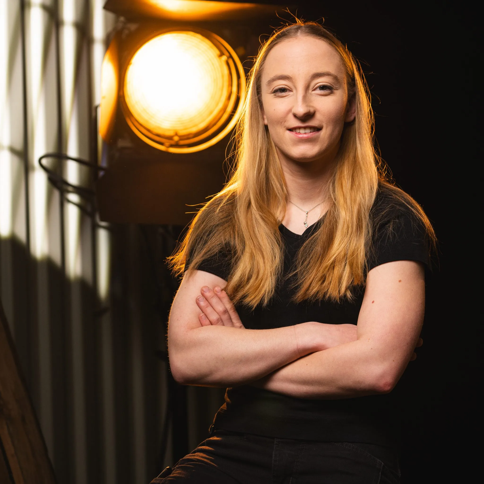 hanna Roder mit langen blonden Haaren, trägt eine Schwarzes T-shirt lächelt in die Kamera, eine Stufenlinse steht hinter ihm