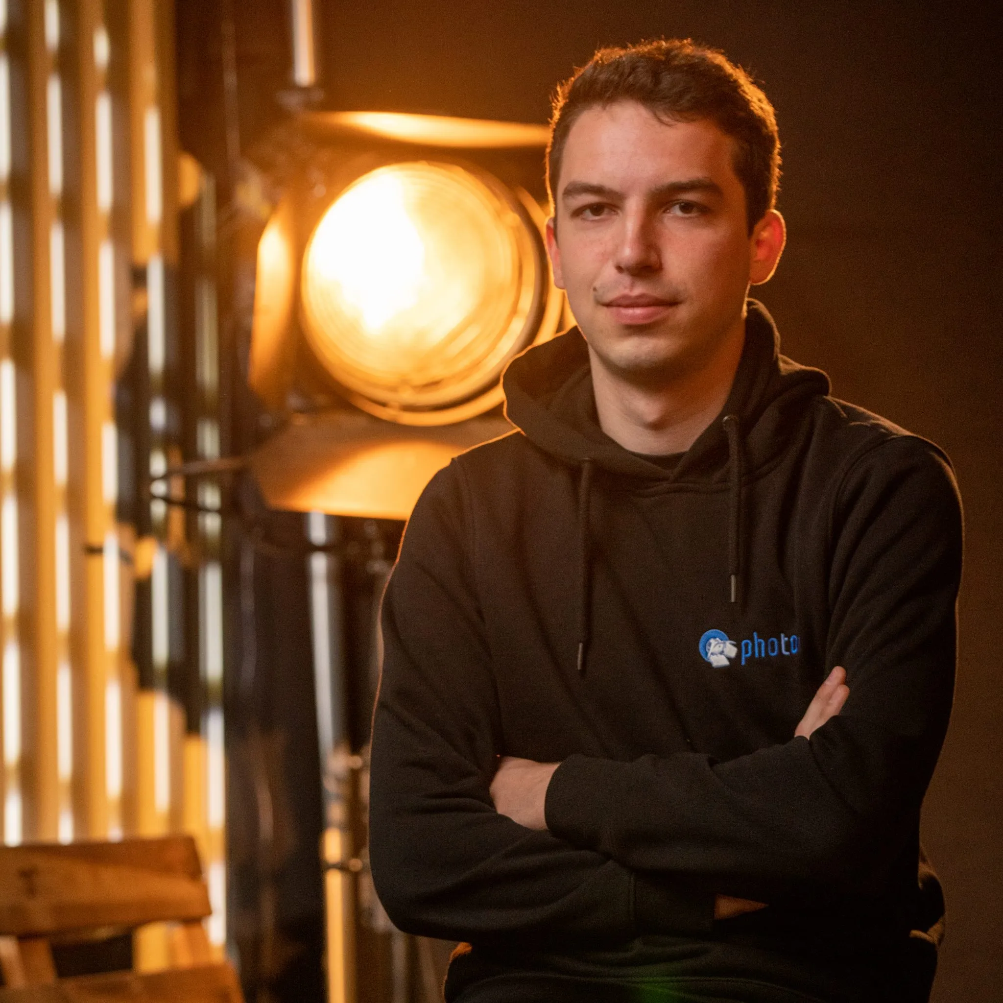Jakob Nonn mit schwarzen Haaren, trägt einen Schwarzen Hoody lächelt in die Kamera, eine Stufenlinse steht hinter ihm