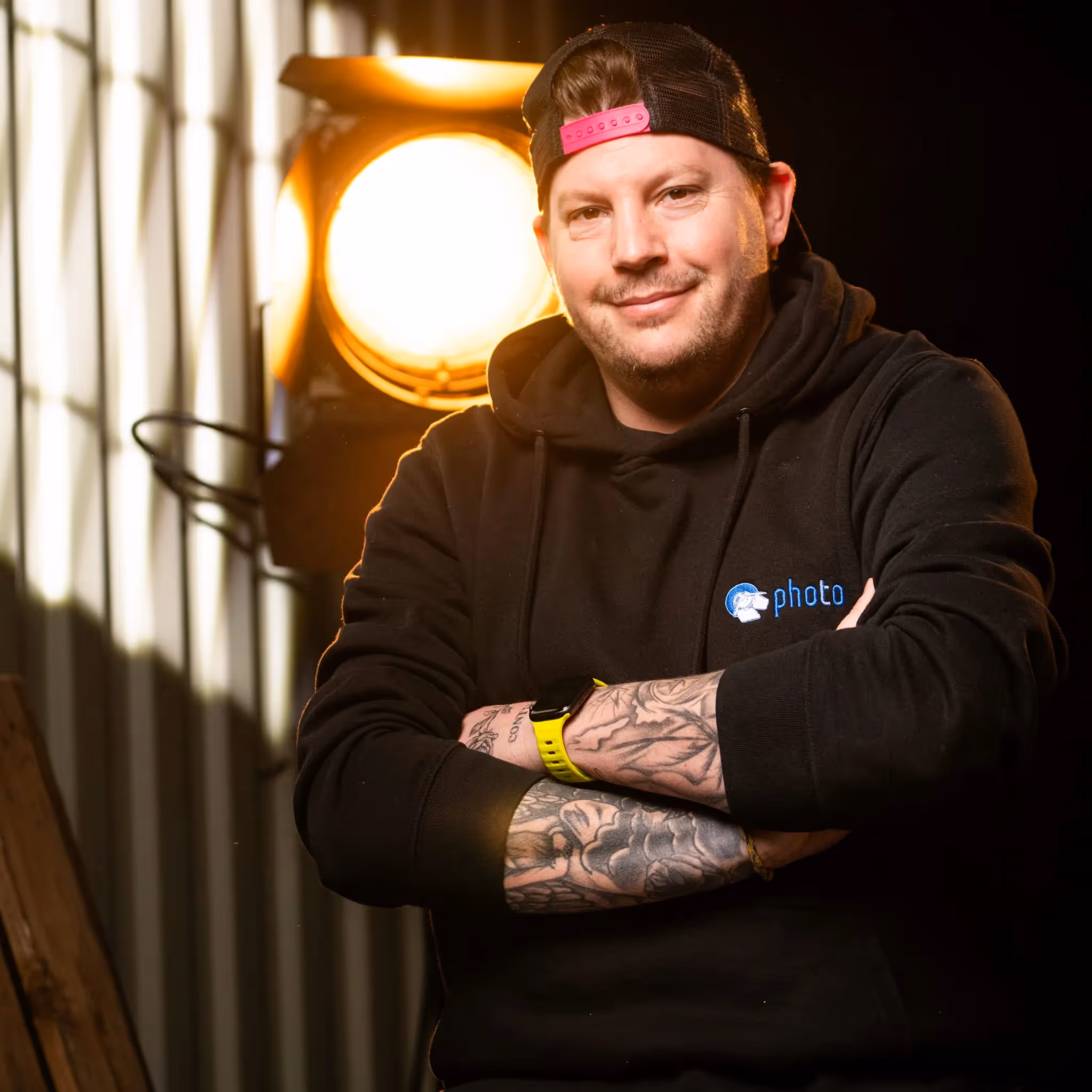 Daniel Breidenbach mit schwarzen Haaren, trägt einen Schwarzen Hoody lächelt in die Kamera, eine Stufenlinse steht hinter ihm
