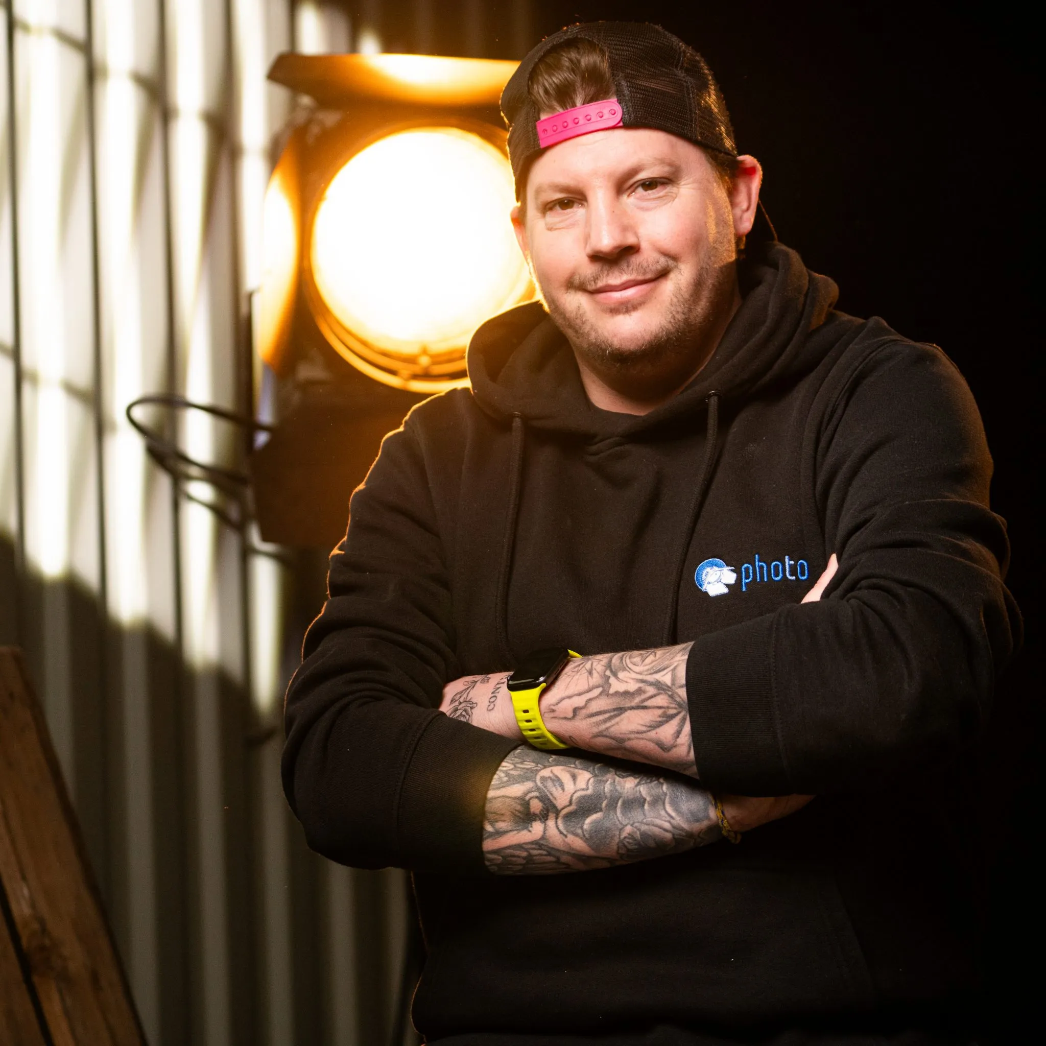 Daniel Breidenbach mit schwarzen Haaren, trägt einen Schwarzen Hoody lächelt in die Kamera, eine Stufenlinse steht hinter ihm