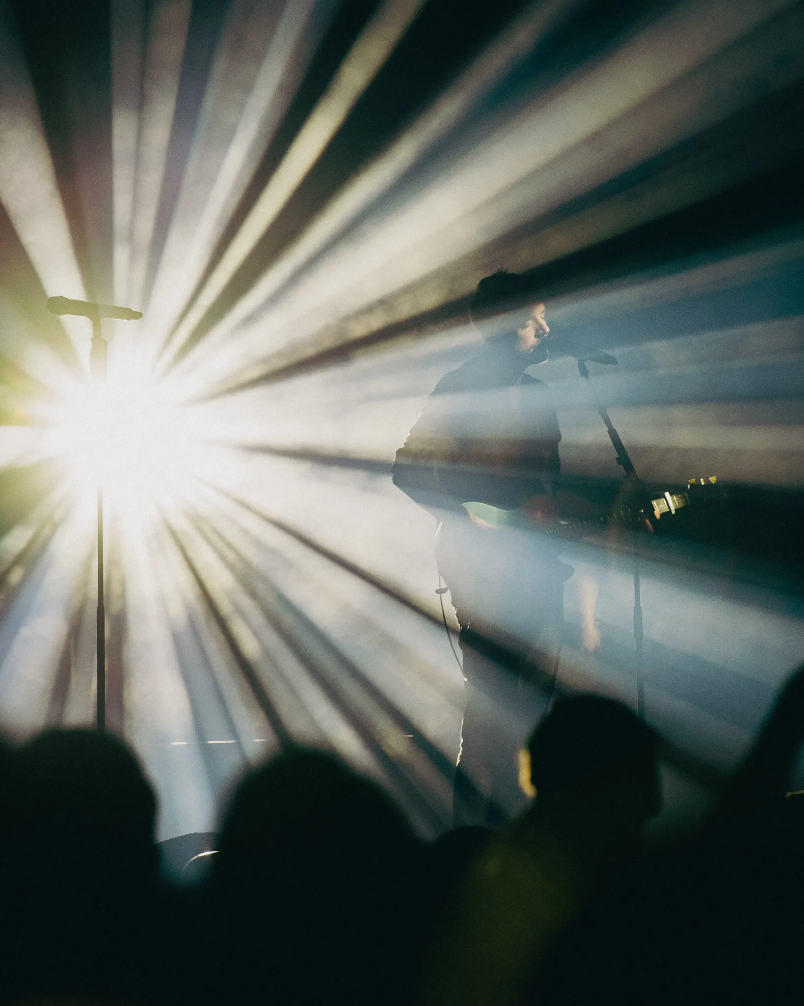 Ein Sänger sing in ein Mikrofon und wird von hinten mit Lichttechnik mit verschiedenen Strahlen angeleuchtet