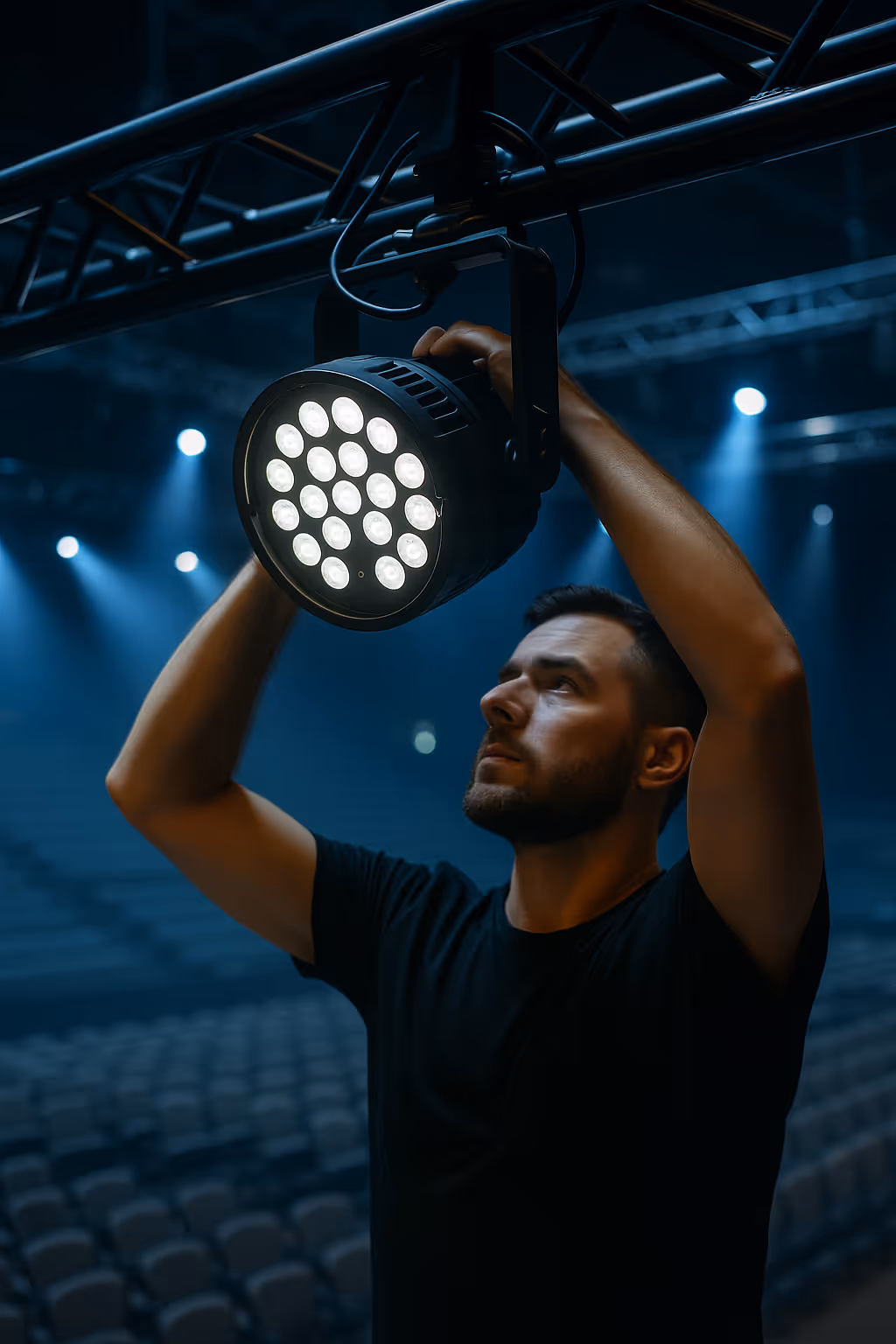 Ein beleuchter leuchtet einen LED Scheinwerfer ein. im Hintergrund ist eine Bühne zu sehen