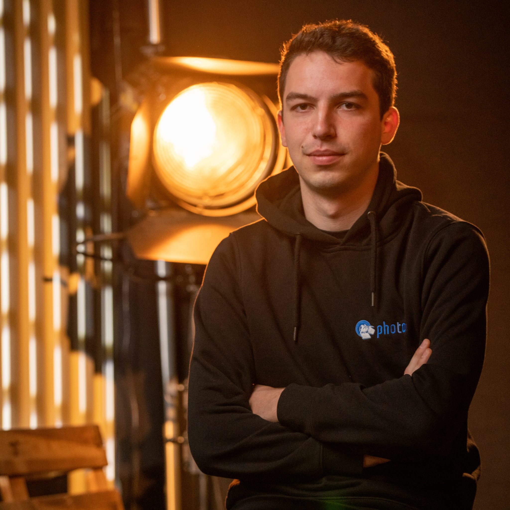 Jakob Nonn mit schwarzen Haaren, trägt einen Schwarzen Hoody lächelt in die Kamera, eine Stufenlinse steht hinter ihm