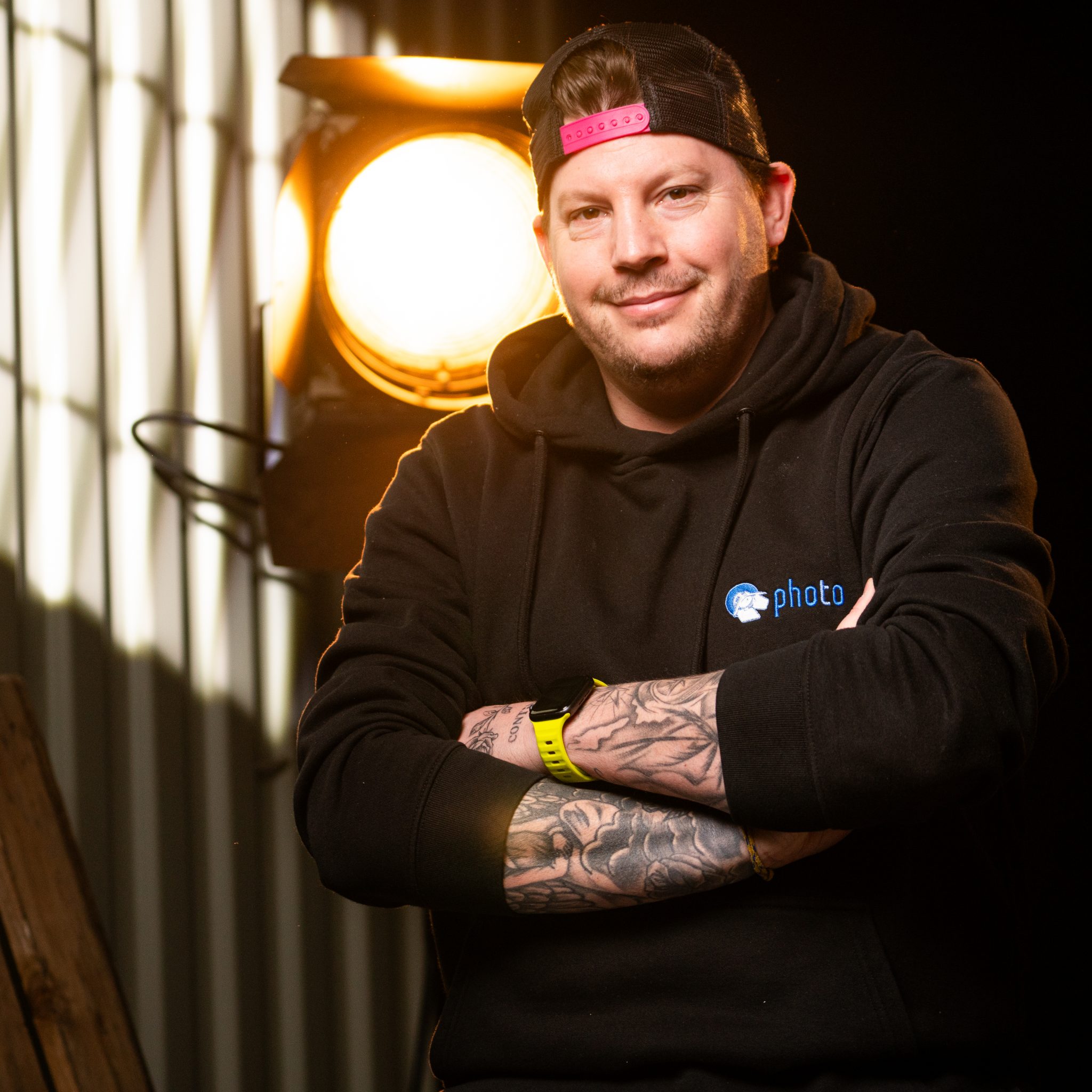 Daniel Breidenbach mit schwarzen Haaren, trägt einen Schwarzen Hoody lächelt in die Kamera, eine Stufenlinse steht hinter ihm