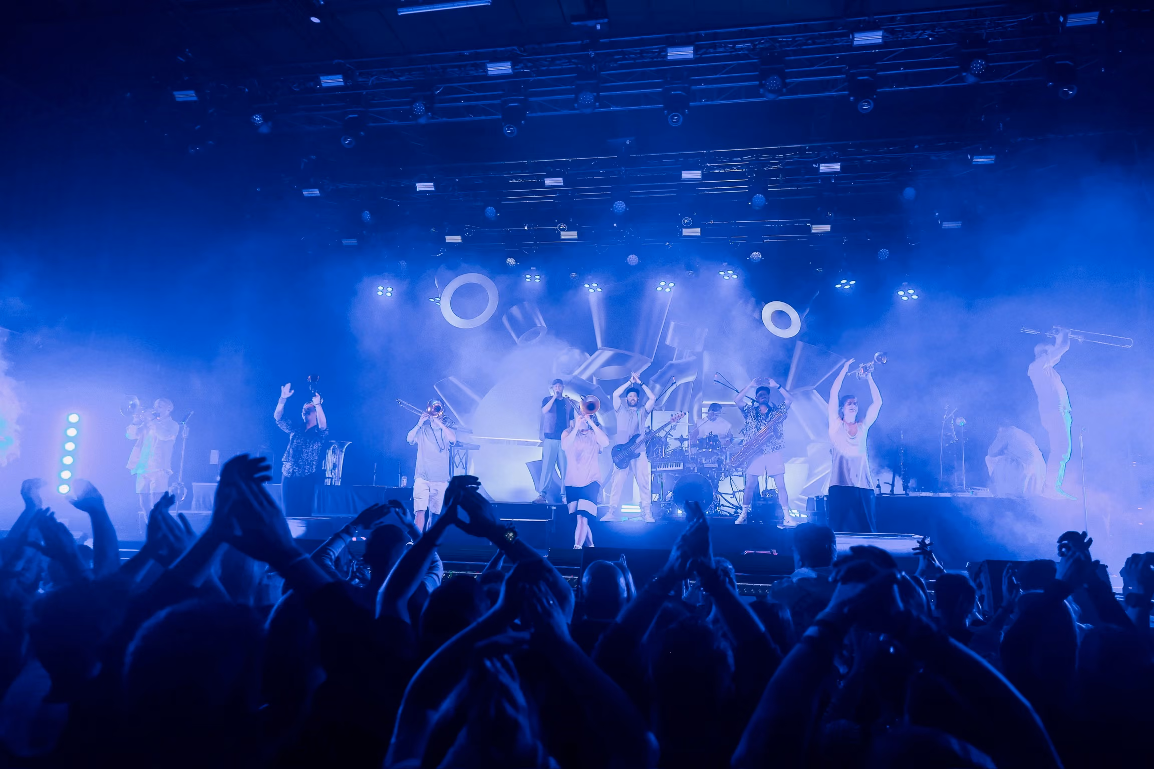 A brass band on stage seen centrally from the audience, lit by photon