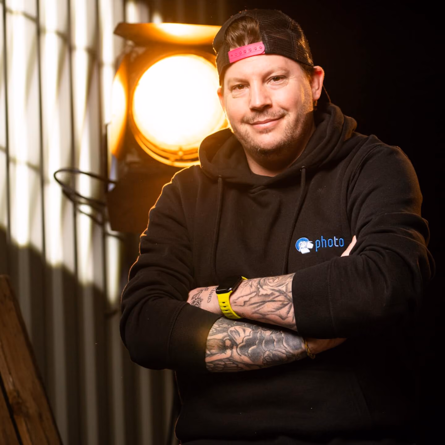 Daniel Breidenbach mit schwarzen Haaren, trägt einen Schwarzen Hoody lächelt in die Kamera, eine Stufenlinse steht hinter ihm