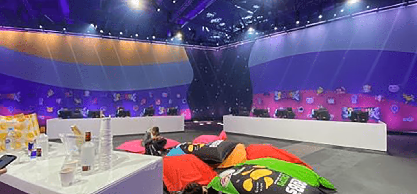 A long table lined with swivel chairs and a PC at each spot, white light beams from above and a colourful banner behind, by photon