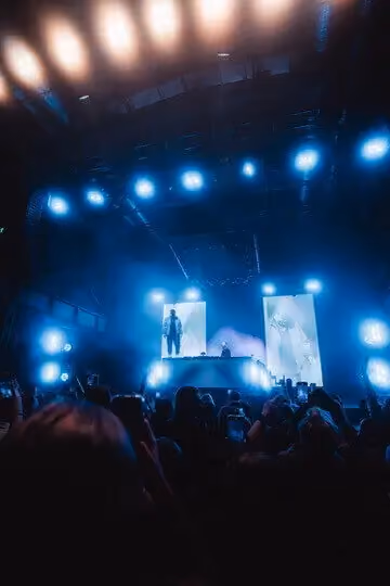 Eine Große Gruppe von leuten schaut einem DJ bei seiner Show zu. Im hintergrund ist eine LED wand zu sehen die drei Köpfe Zeigt in weiss.
