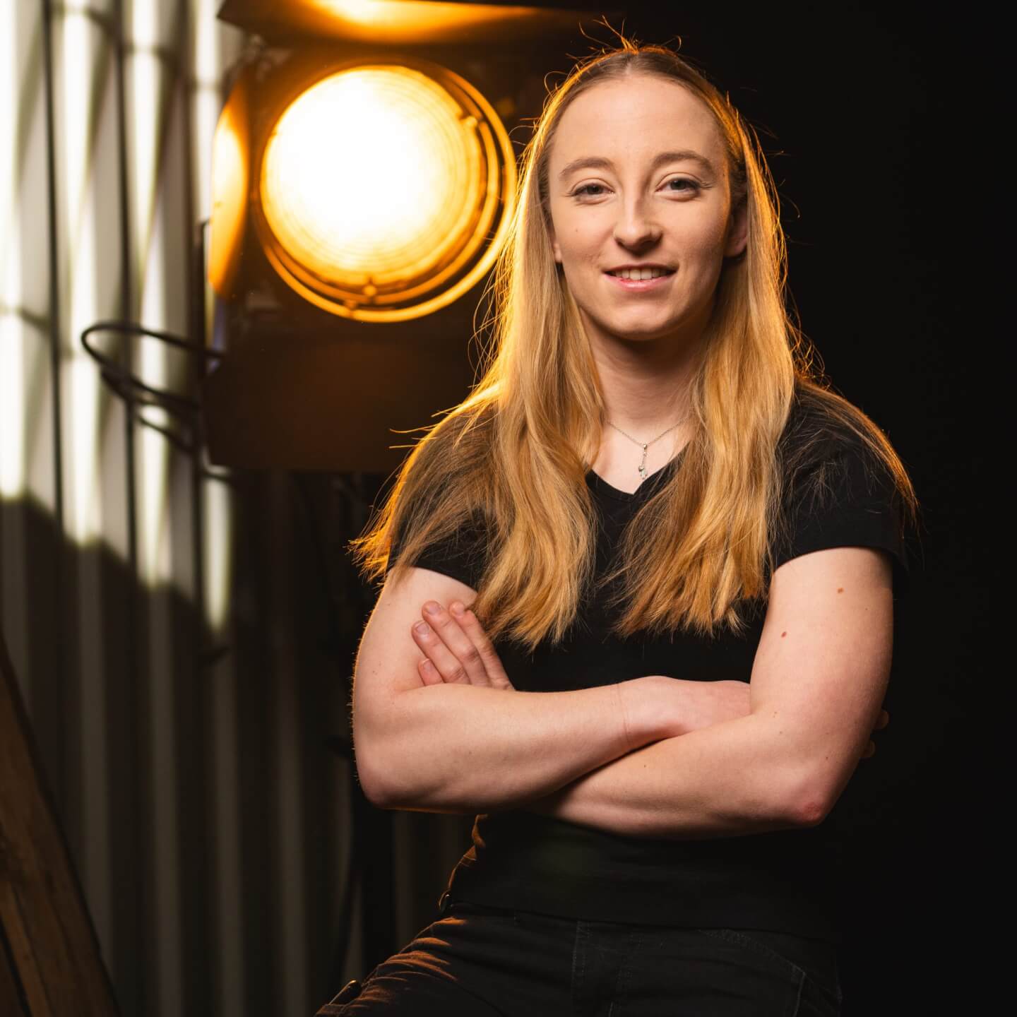 Hanna Roder mit langen blonden Haaren, trägt ein schwarzes T-Shirt, lächelt in die Kamera, eine Stufenlinse steht hinter ihr