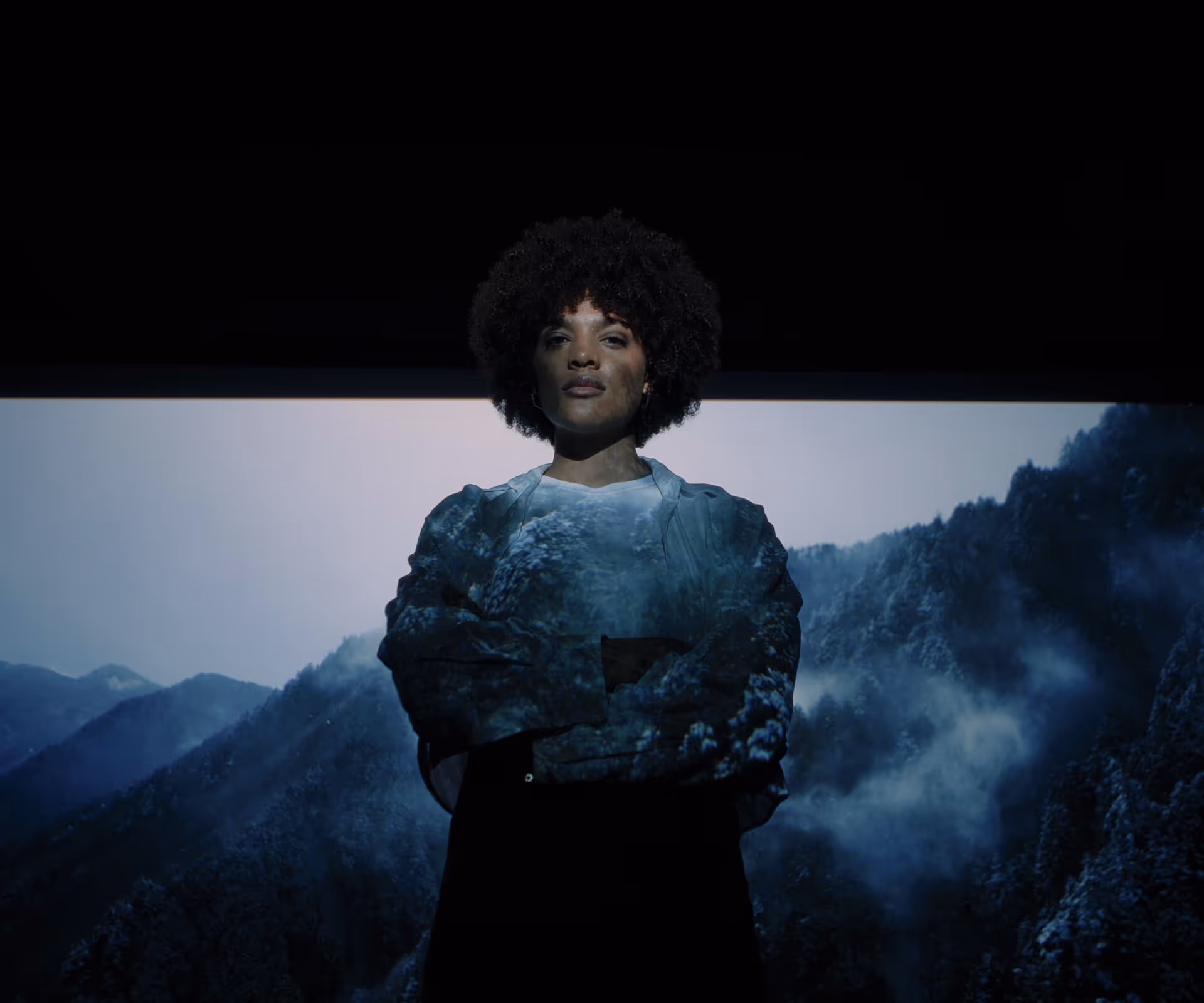 Portrait of a woman with an afro in front of a projection of snow-covered mountain landscapes — key visual for Volvo eZone electric mobility, realized by the Viennese full-service agency Achtzehn Grad for Volvo Austria.