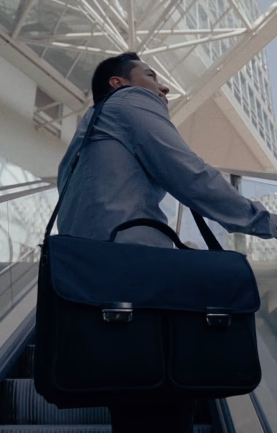 Geschäftsmann mit Aktentasche auf einer Rolltreppe in einem modernen, lichtdurchfluteten Gebäude.
