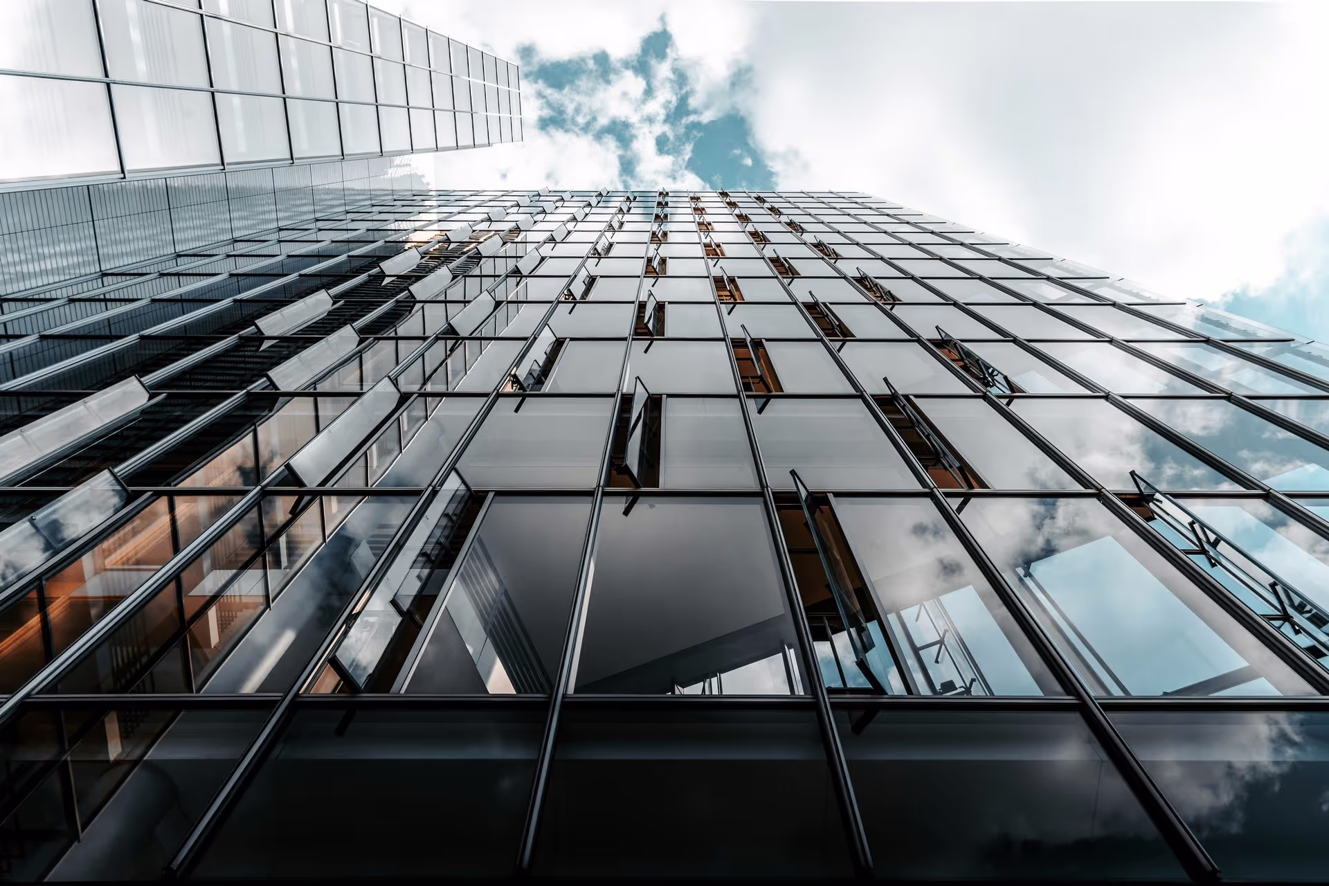 A modern glass building reflects the sky, showcasing large windows and a sleek design, creating a striking architectural perspective.