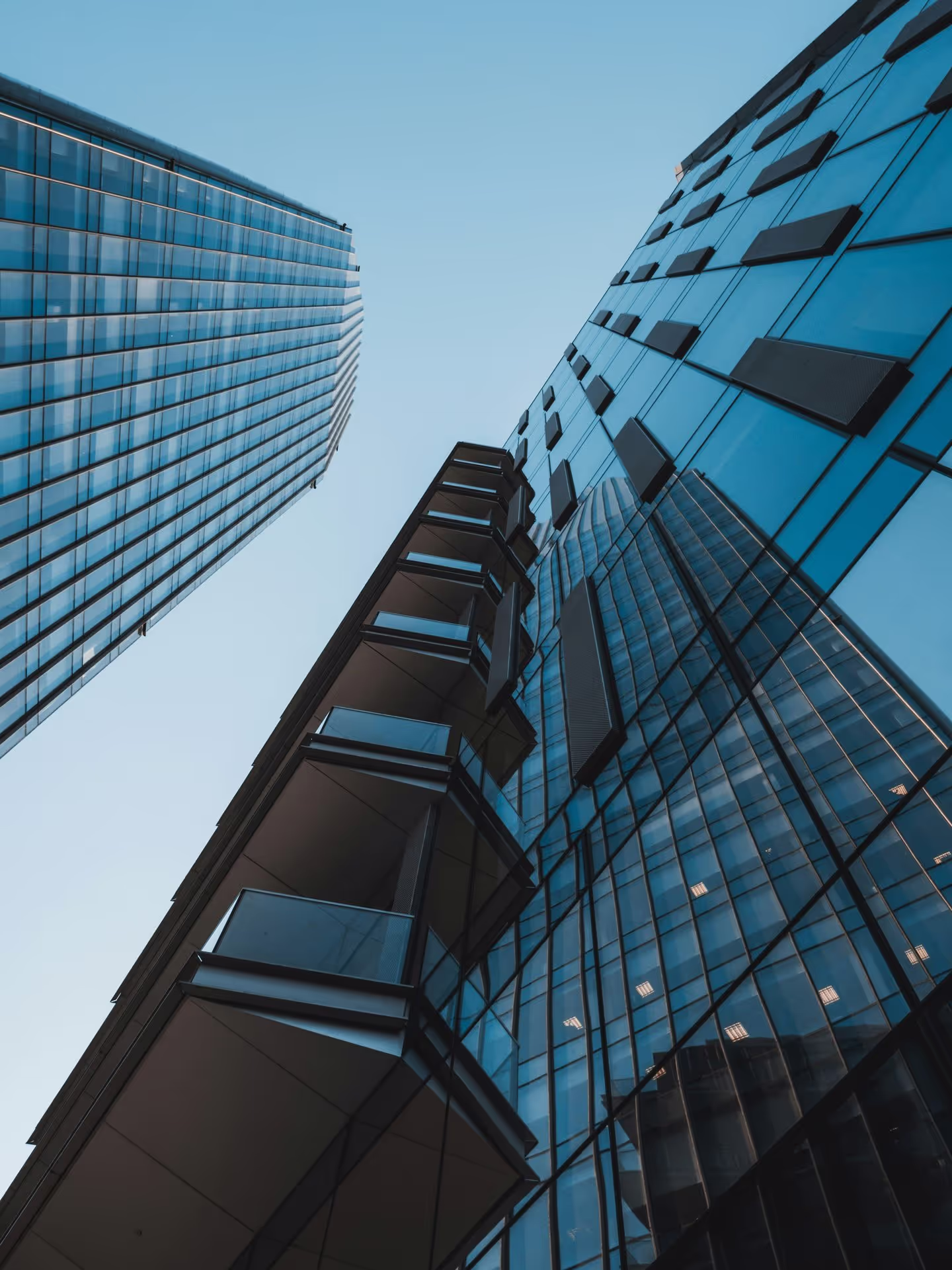 Looking up at modern skyscrapers with reflective glass facades against a clear blue sky, showcasing contemporary architectural design.