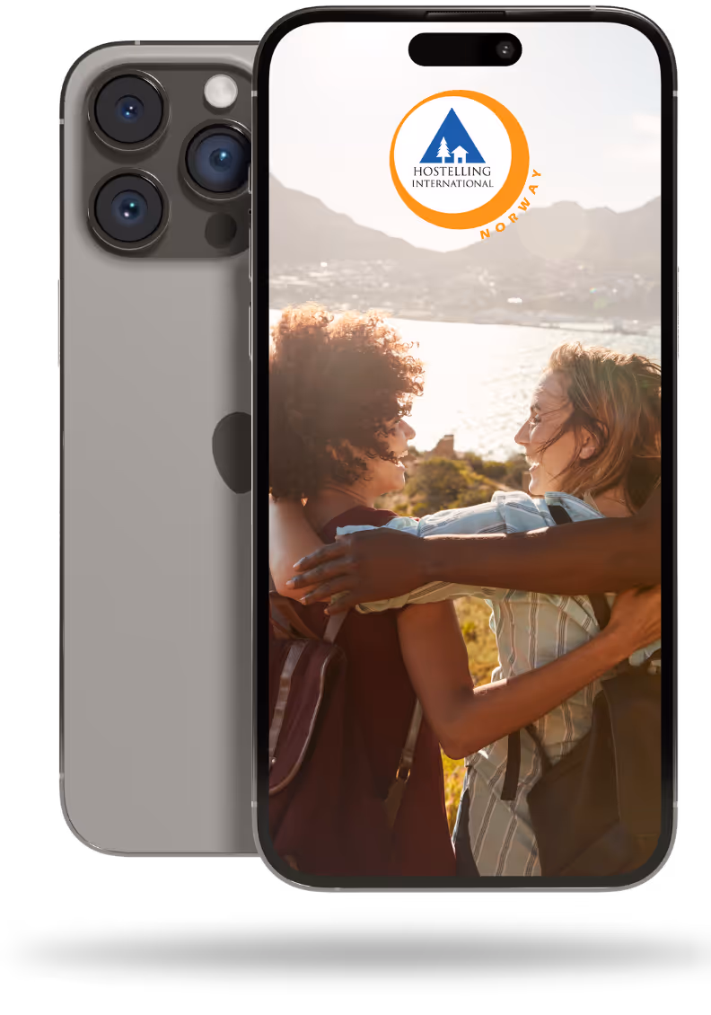 En telefon viser to personer som smiler med armene rundt hverandre, stående utendørs med fjell og vann i bakgrunnen. Logoen til Hostelling International Norge er synlig øverst på skjermen.