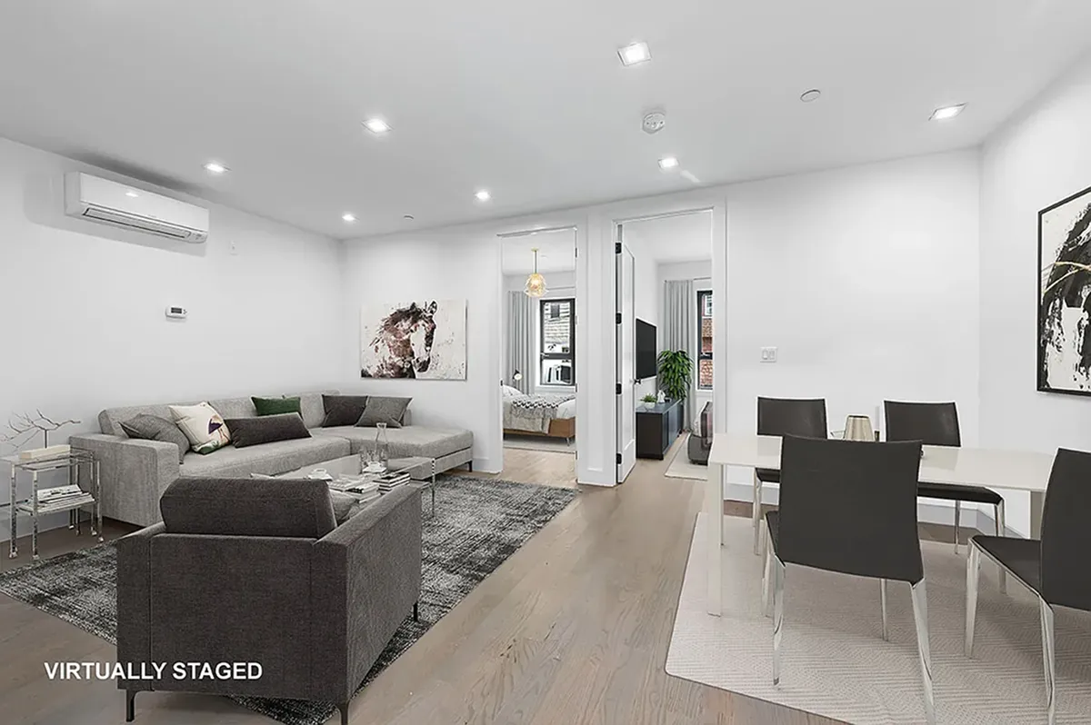 Modern living room with gray sectional sofa, single armchair, glass coffee table, and dining area with black chairs and white table.