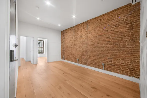 Empty room with wooden floor, exposed brick wall, white walls, and ceiling lights.