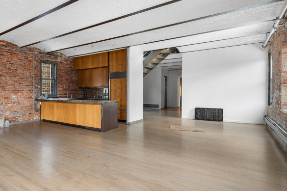 Spacious loft with exposed brick walls, wooden kitchen island, hardwood floors, and white ceiling beams.