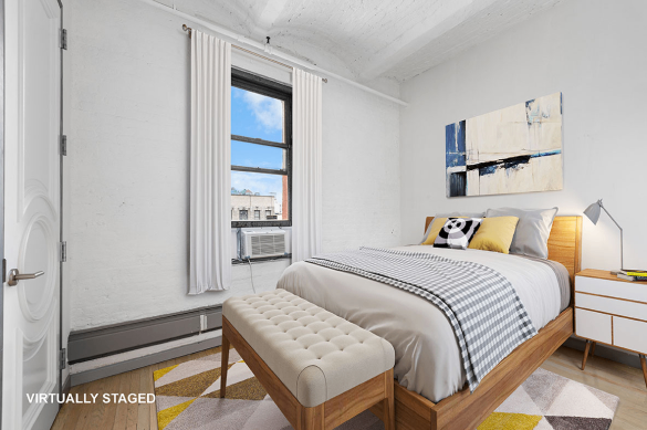 Modern bedroom with wooden bed frame, gray and white bedding, decorative pillows, a beige cushioned bench, white nightstand with lamp, and abstract wall art.