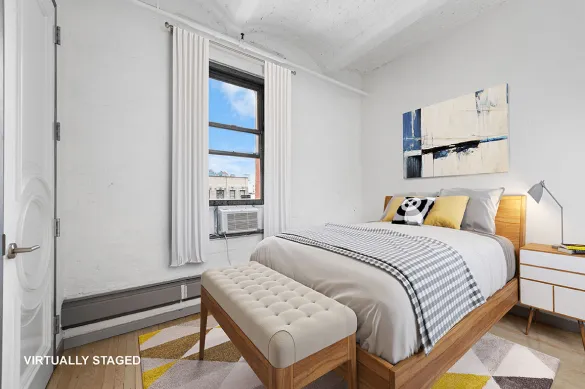 Modern bedroom with wooden bed frame, gray and white bedding, decorative pillows, a beige cushioned bench, white nightstand with lamp, and abstract wall art.
