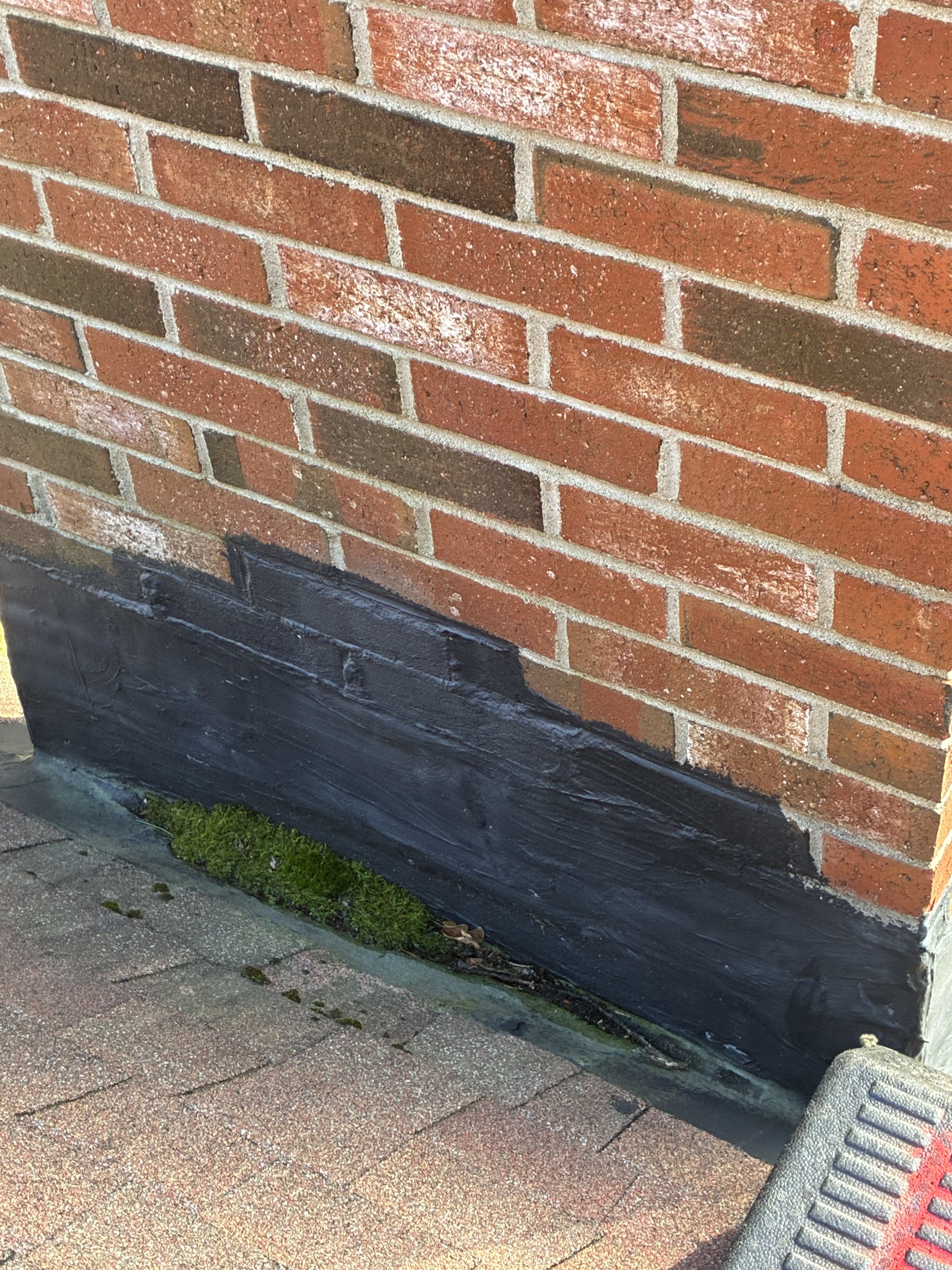 Brick chimney base with patched flashing and moss buildup where the chimney meets the roof – exterior damage found during a chimney repair estimate