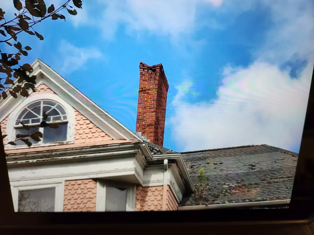Tall chimney on a Victorian home with a crumbling, damaged top before rebuild