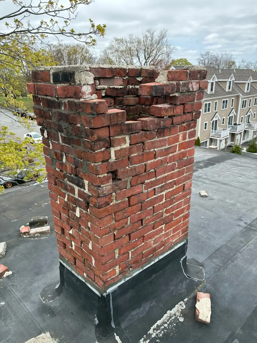 Chimney with spalling, broken bricks and a crumbling top on a flat roof