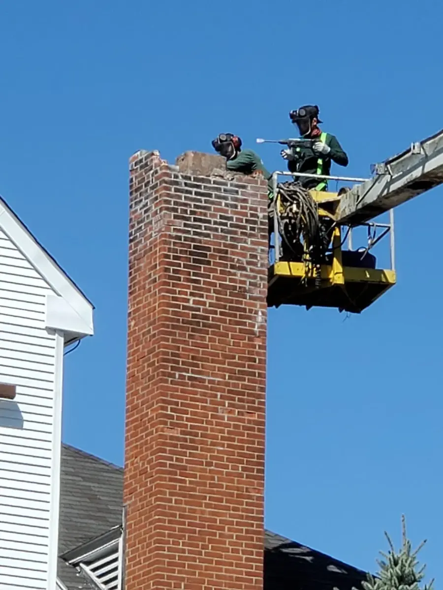Dave's Chimney Service crew taking down a tall brick chimney from a lift
