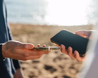 Two people holding smartphones close together to complete a mobile transaction by the beach.