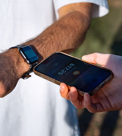 Close-up of a person using a mobile phone to make a payment via a smartwatch on another person's wrist.