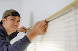 man measuring curtains to be hung to a wall and window