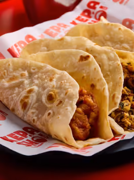 Three soft tacos with different fillings on branded paper in a black tray.