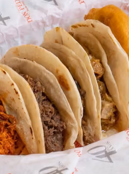 Close-up of four tacos with different meats and an onion ring on the side.