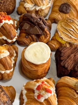Assortment of decorated croissants and pastries with chocolate, cream, and other toppings.