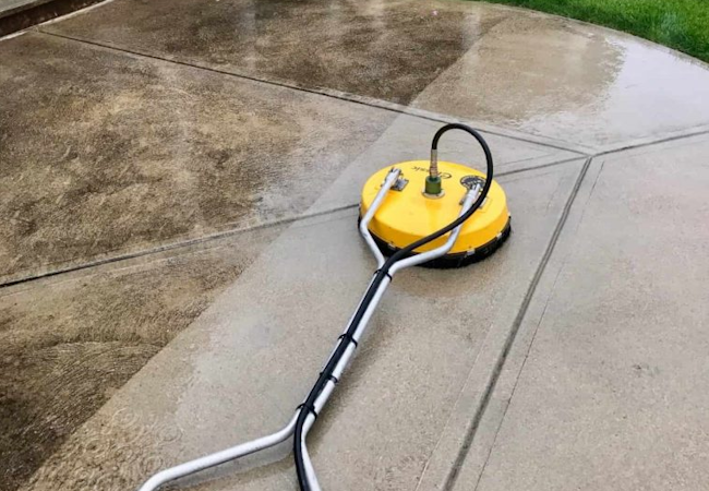 Yellow rotary surface cleaner on a concrete driveway, dirty and cleaned halves visible