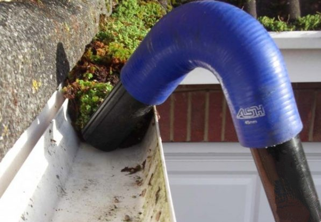 Blue vacuum nozzle lifting moss and leaf debris out of a house gutter