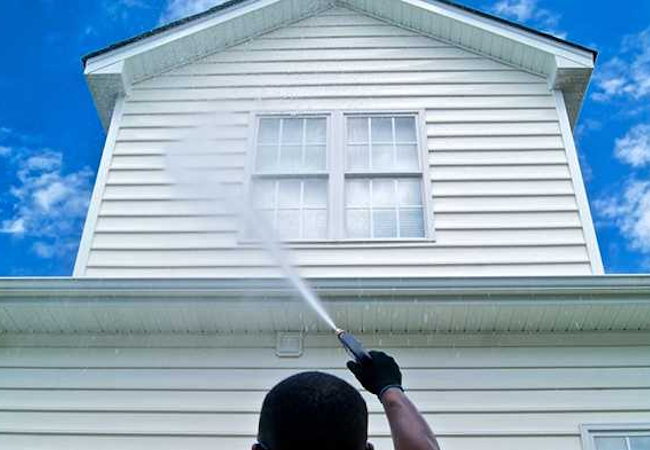 Cleaner spraying a wide fan of water across white weatherboard cladding and gable