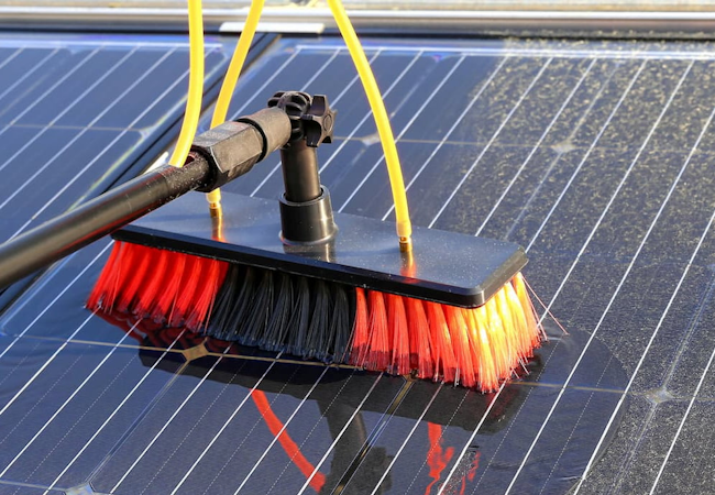 Red and black brush head on a pole scrubbing a wet solar panel