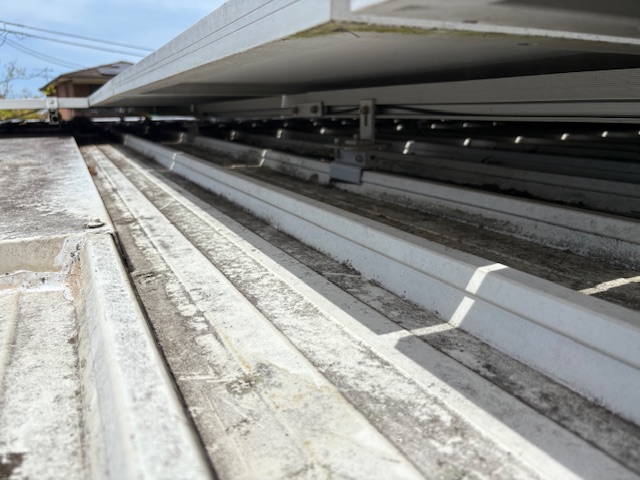 Low angle beneath solar panel frames showing grimy corrugated roof sheeting underneath