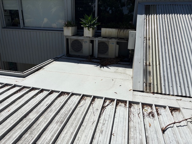 Rooftop air conditioning units and potted plants above a leaf-scattered metal roof