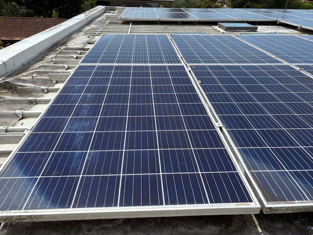 Dusty solar panels on a flat roof with a tiled house roof behind