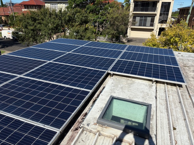 Rooftop solar panels beside a skylight with an apartment block behind