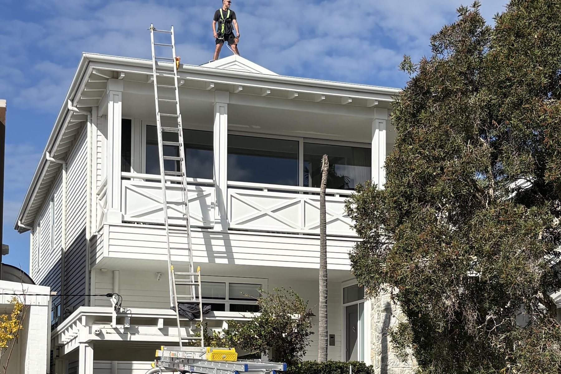 Extension ladder set against a two-storey white weatherboard Sydney home reaching the gutter line, with an Ultimate Exterior Clean truck at the kerb.
